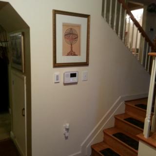 A view of a staircase in a hallway with a picture frame and thermostat on the wall.
