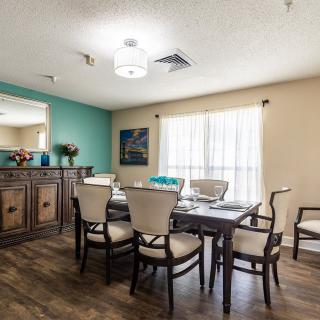 A well-lit dining area with a wooden table and chairs, featuring artwork and decorative elements.