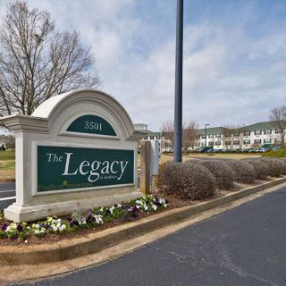 Entrance sign for The Legacy Apartments with surrounding landscaping.