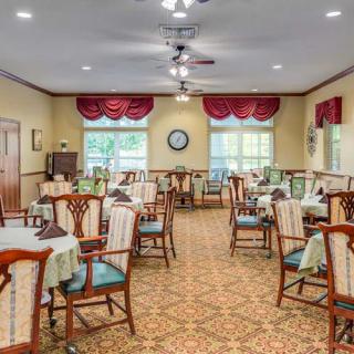 A cozy dining room with neatly arranged tables and chairs, decorated with elegant curtains and a patterned carpet.
