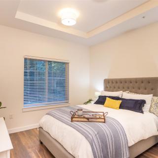 A cozy and modern bedroom featuring a neatly made bed with layered bedding and decorative pillows, complemented by a large window.