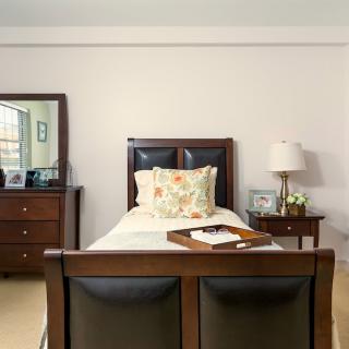 A cozy bedroom with a wooden bed, nightstand, and dresser, featuring a decorative lamp and mirror.