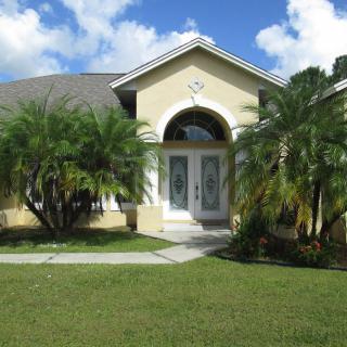 A suburban house with palm trees and a well-manicured front yard on a sunny day.