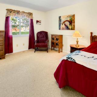 A cozy bedroom featuring a bed with a red comforter, a wooden dresser, and a window with curtains.