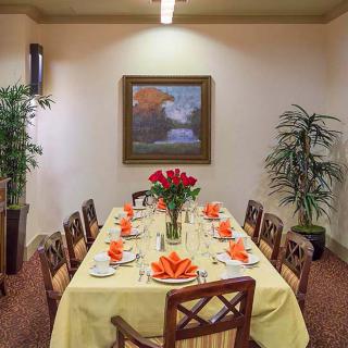 A beautifully set dining table with a centerpiece of red flowers, surrounded by elegant chairs in a warmly decorated room.