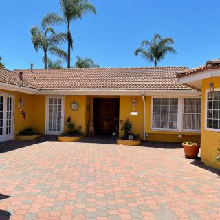 A charming yellow house with a brick courtyard and palm trees in the background under a clear blue sky.