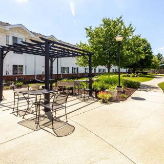 A sunny outdoor area featuring a pergola with tables and chairs surrounded by a landscaped garden.