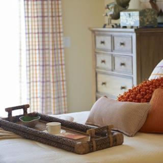 A cozy bedroom setting featuring a wooden tray on the bed adorned with decorative pillows.