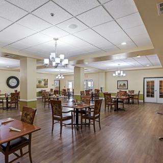 An empty dining room with neatly arranged tables and chairs, featuring chandeliers and wooden flooring.