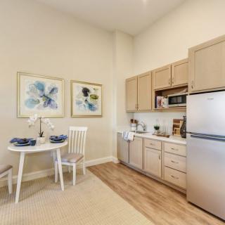 A cozy kitchenette with light wood cabinets, a compact dining area, and decorative artwork.