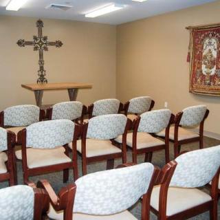 A small chapel with neatly arranged chairs facing a cross on the wall.