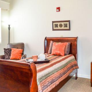 A cozy bedroom featuring a wooden sleigh bed with a colorful quilt and decorative pillows, complemented by an armchair and wall art.