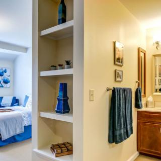 A cozy bedroom with adjacent bathroom featuring open shelves and blue accents.
