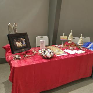 A festive table display featuring handmade holiday decorations and artwork at a craft fair.