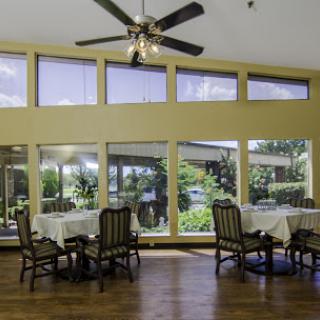 A bright and spacious dining area featuring large windows that provide ample natural light and a view of the surrounding greenery.