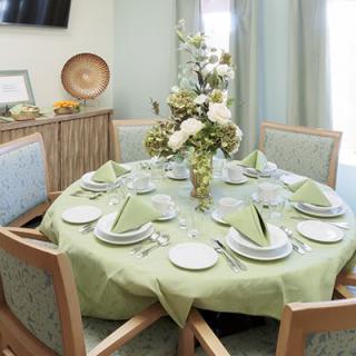 A beautifully set dining table with a green tablecloth and a centerpiece of flowers, surrounded by wooden chairs.