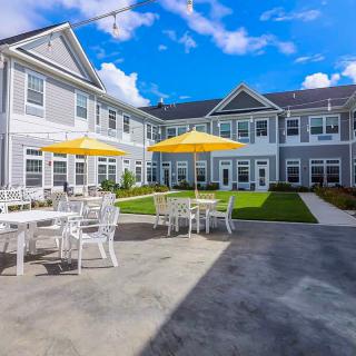 A sunny day at a residential building with outdoor seating and umbrellas in the courtyard.