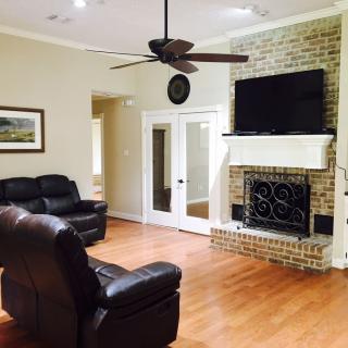 A cozy living room featuring leather seating, a brick fireplace with a mounted TV, and wooden floors.