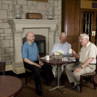 Three elderly men enjoying a conversation around a table with coffee in a cozy indoor setting.