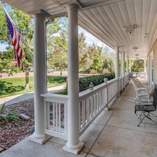 A serene porch view featuring classic columns, outdoor seating, and a waving American flag against a backdrop of lush greenery.