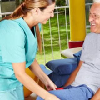 A nurse is attending to an elderly man outdoors, both are smiling during the interaction.