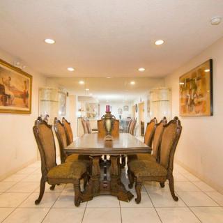 Elegant dining room with a large wooden table and ornate chairs, surrounded by artwork and soft lighting.