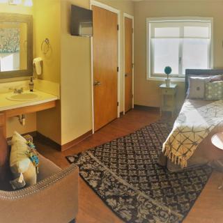 A cozy bedroom with a neatly made bed, decorative rug, and a window letting in natural light.