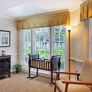 A cozy living room with a large window, featuring a desk and chairs, a floor lamp, and elegant curtains.
