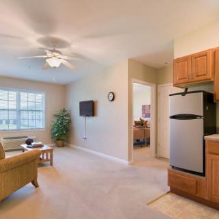 A modern apartment living room with a cozy sofa, wall-mounted TV, and open kitchen area featuring a stainless steel refrigerator.