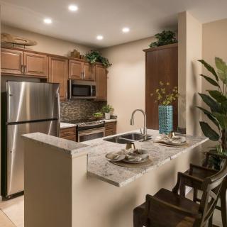 A modern kitchen featuring stainless steel appliances, wooden cabinets, and a cozy seating area with bar stools.