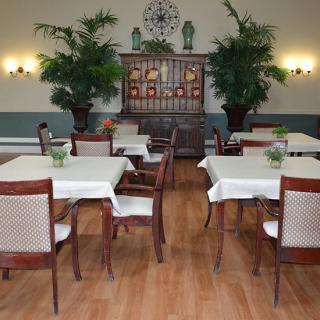 A cozy dining room with neatly arranged tables and chairs, decorated with indoor plants and wall lamps.