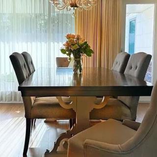 A beautifully set dining room with an elegant table adorned with a flower centerpiece and surrounded by upholstered chairs beneath a sparkling chandelier.