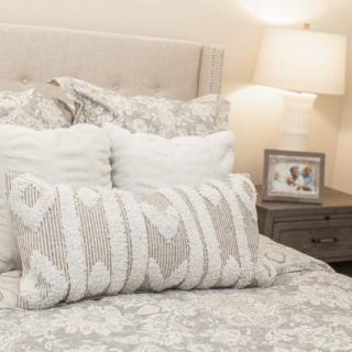 A cozy bedroom featuring a neatly made bed with decorative pillows, a nightstand with a lamp, and a framed photo.