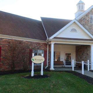 A brick building with a columned entrance and a sign on the lawn.