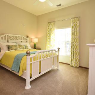 A bright and cozy bedroom with a white bed, colorful bedding, and large window curtains.