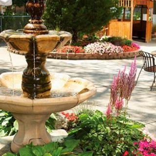 A beautifully designed fountain surrounded by vibrant flowers and lush greenery in a serene outdoor setting.