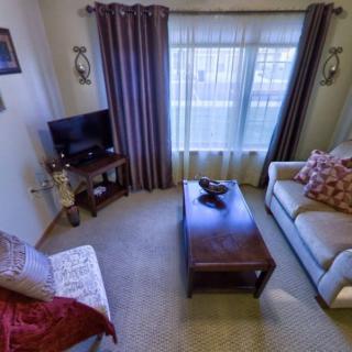 A cozy living room featuring a sofa, armchair, and coffee table, with a television in the corner near the window dressed with curtains.
