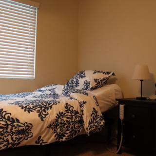 A cozy bedroom with a neatly made bed, featuring a patterned duvet and pillows, next to a nightstand with a lamp.