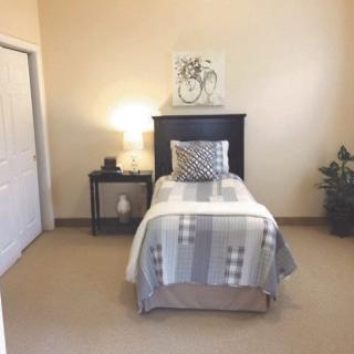 A cozy bedroom with a single bed, nightstand, lamp, and decorative elements.