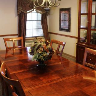 A traditional dining room with a wooden table, chairs, and a chandelier, featuring a floral centerpiece.