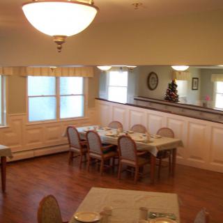 A cozy dining room setup with tables and chairs, featuring soft lighting and wooden flooring.