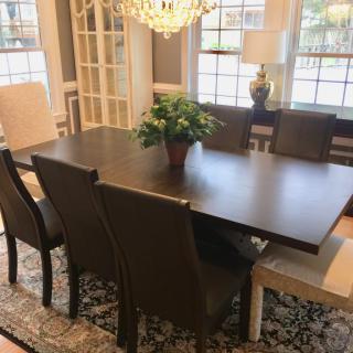 A well-furnished dining room featuring a large wooden table with chairs, a decorative chandelier, and natural lighting from the windows.