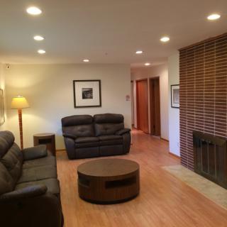 A cozy living room featuring leather sofas, a round coffee table, and recessed lighting with a wooden floor and fireplace.