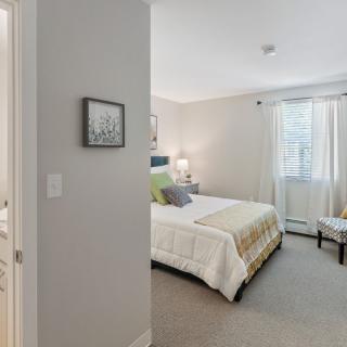 A cozy bedroom with a neatly made bed, soft lighting, and a window providing natural light.