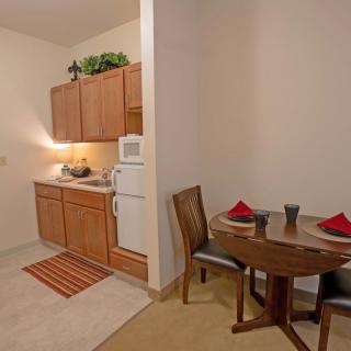 A compact kitchen area with wooden cabinets, a small dining table, and chairs, ideal for apartment living.