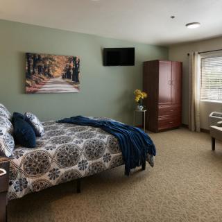 A cozy bedroom with patterned bedding, an armoire, and a wall-mounted TV.