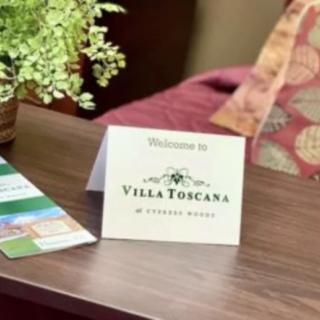 A welcome card from Villa Toscana placed on a table, accompanied by a brochure and a potted plant.