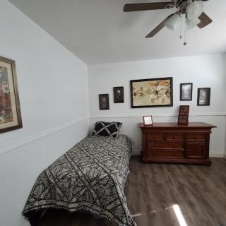 A minimalist bedroom featuring a single bed and wooden dresser with framed artwork on the walls.
