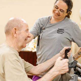 An elderly man receives assistance during a therapy session with a caregiver.