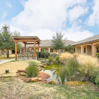 A beautifully landscaped outdoor area featuring a pergola and a small pond surrounded by lush greenery.